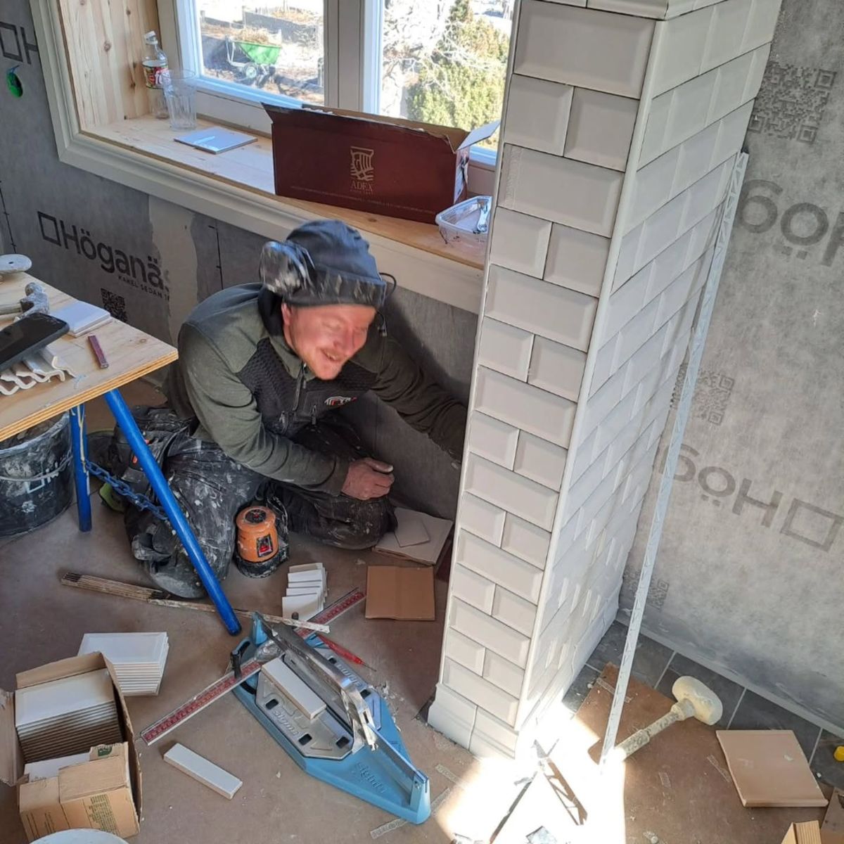 Niclas sätter vitt kakel på en vägg i ett badrum som renoveras.