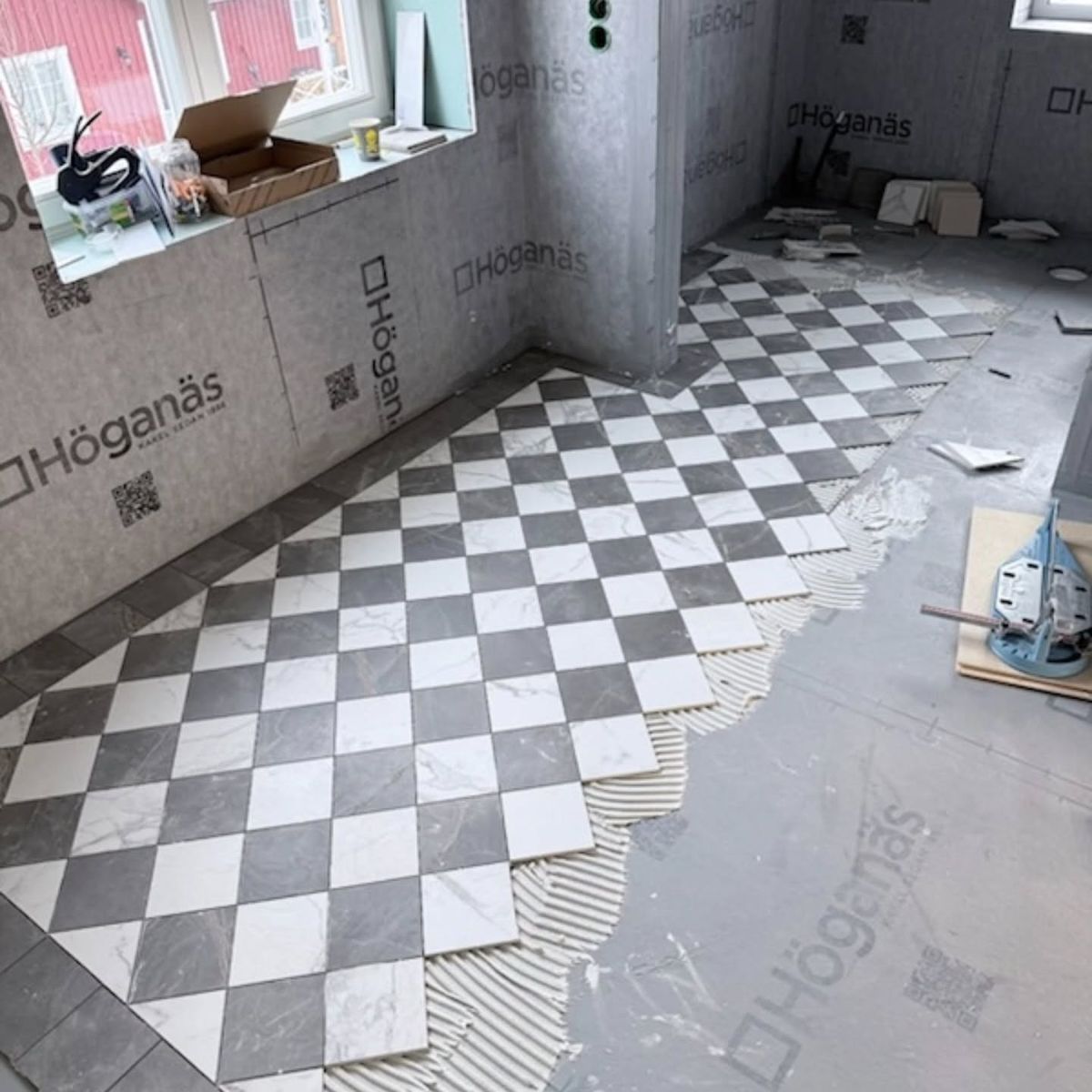 Schackrutigt klinkergolv i svart och vitt som läggs i ett stort badrum.
