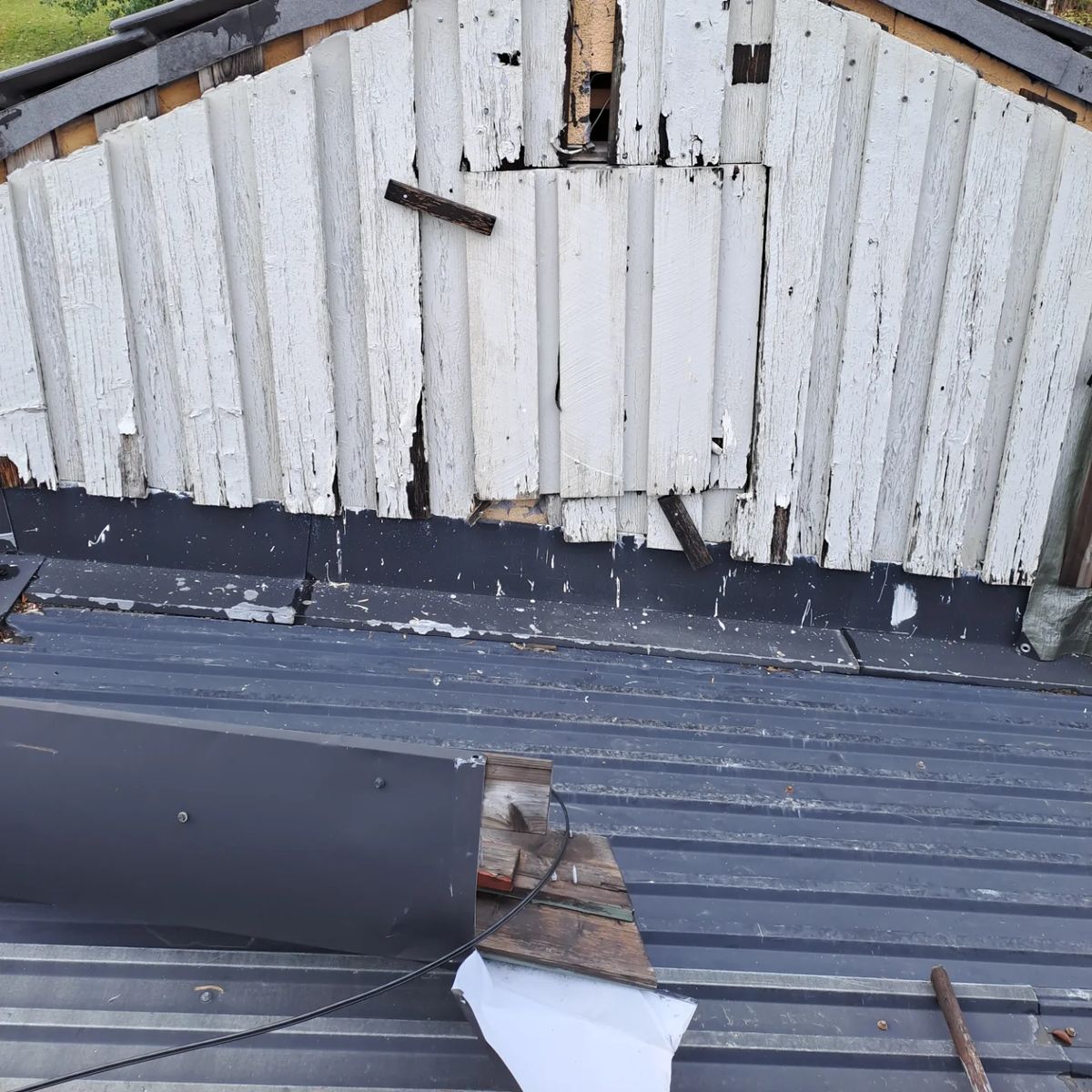 Gavelspets med skadad och flagnande panel innan reparationen.